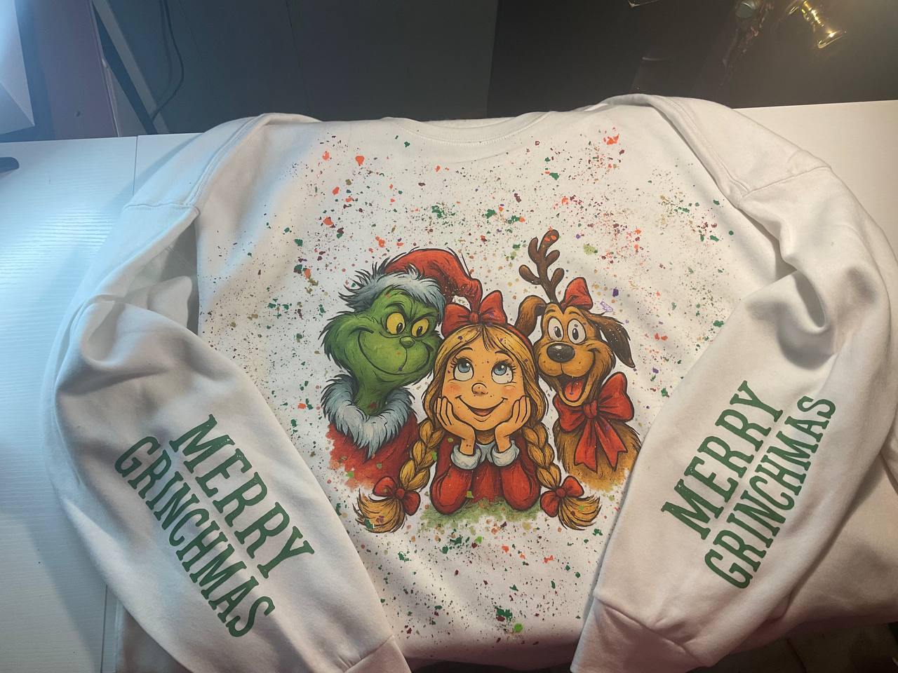 White sweatshirt with Christmas-themed design featuring characters and 'Merry Grinchmas' text.