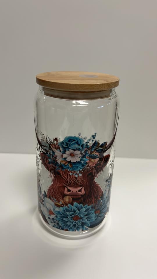 Glass jar with wooden lid featuring a design of a cow and flowers on a white background
