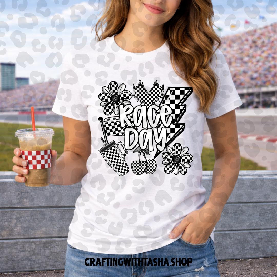 Person wearing a 'Race Day' t-shirt with checkered flags and flowers, holding a drink at a race track.