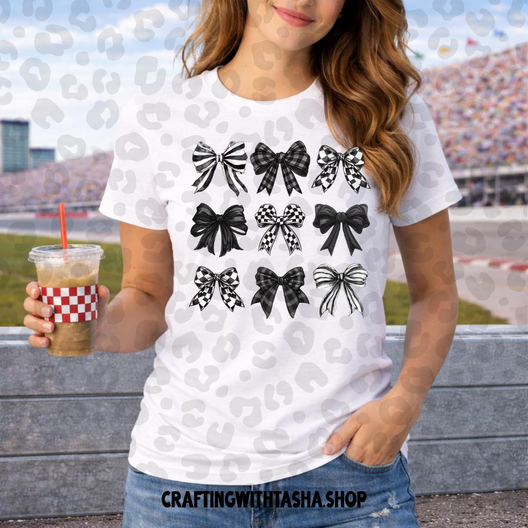 Person wearing a white t-shirt with black bow designs, holding a drink, with a blurred background of a race track.