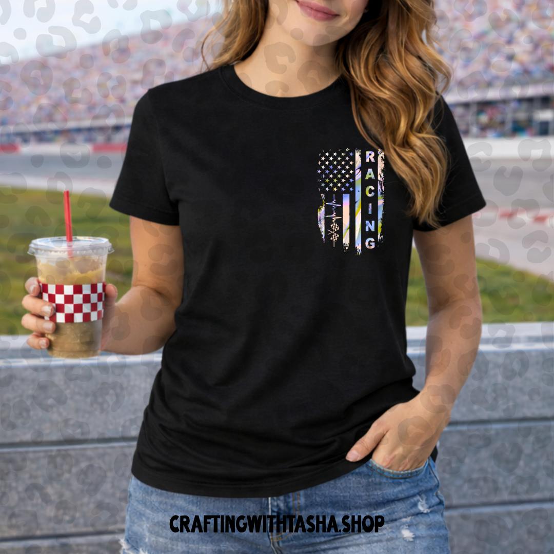 Person wearing a black t-shirt with a graphic design, holding a drink at a race track.