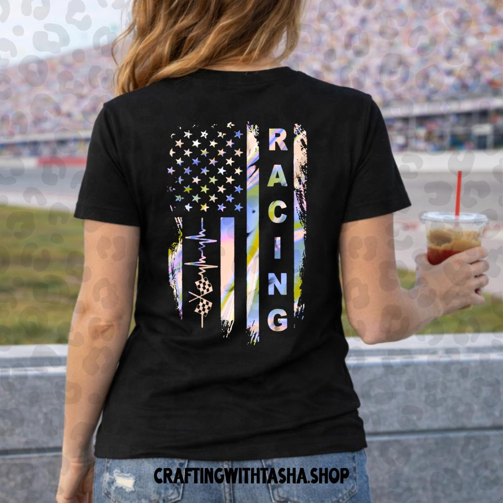 Person wearing a black t-shirt with a colorful American flag design and 'Racing' text, standing at a race track.
