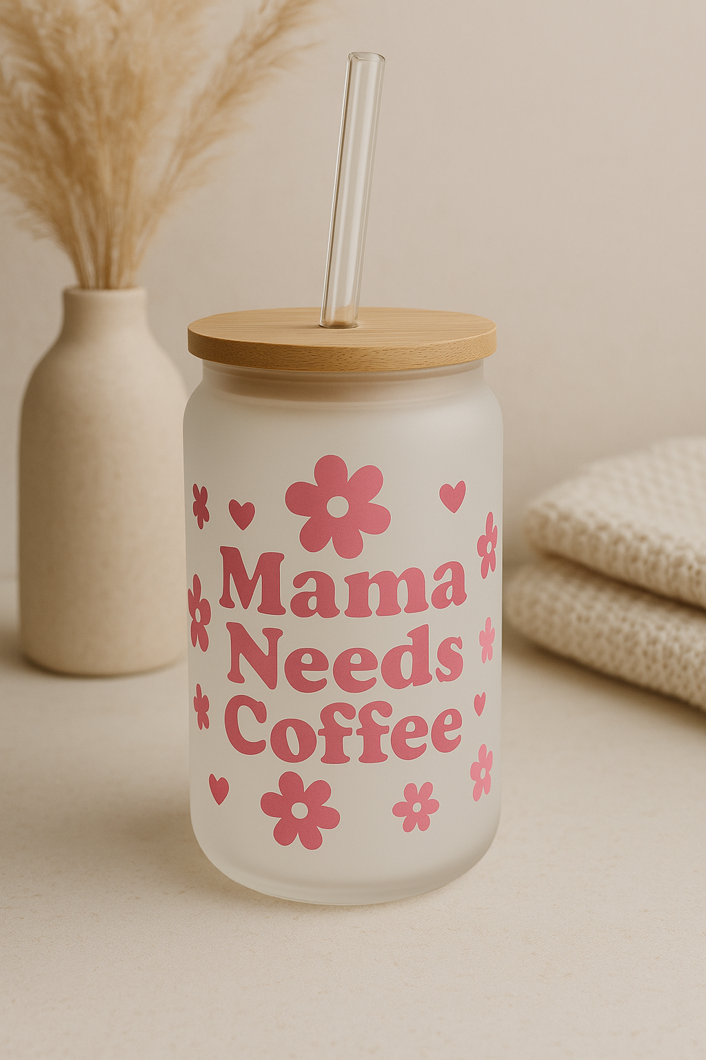Frosted glass tumbler with wooden lid and straw, featuring 'Mama Needs Coffee' text and floral designs on a neutral background.